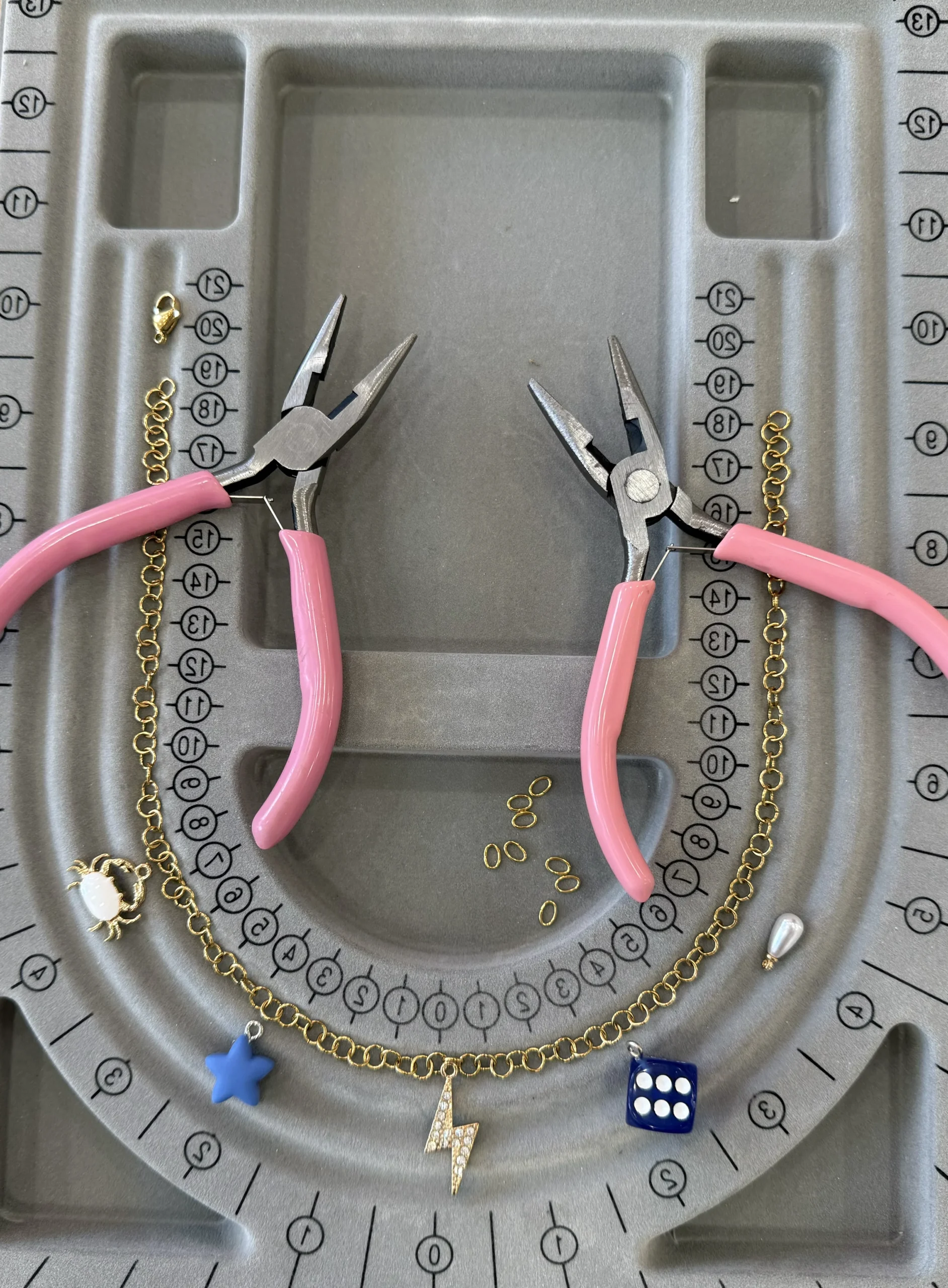 Jewelry making tools and a custom charm bracelet layout on a gray bead mat